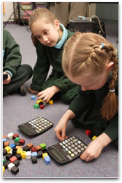 Girls in a classroom using calculators and counting blocks